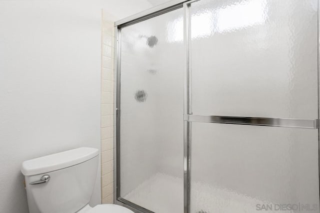 bathroom featuring a shower with door and toilet