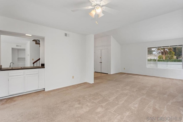 unfurnished living room with ceiling fan, light colored carpet, and sink