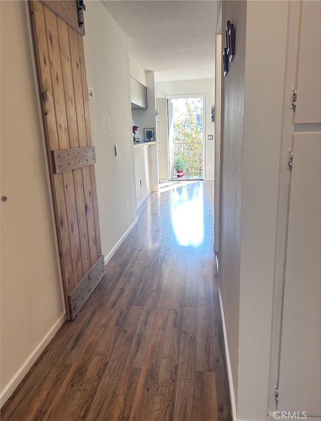 hall with dark wood-type flooring, a barn door, and a textured ceiling