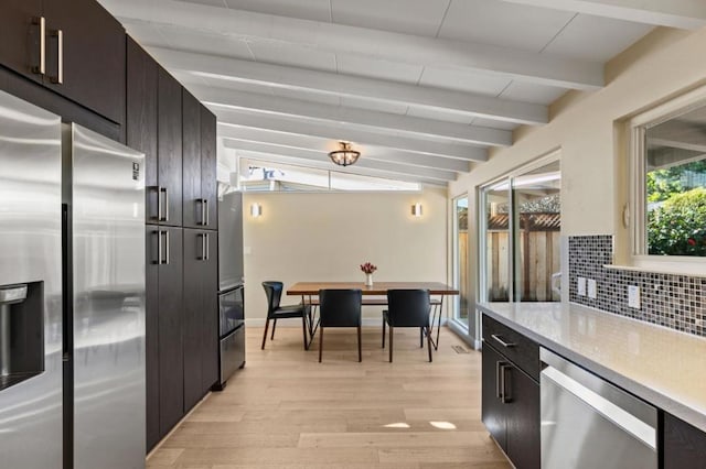 kitchen featuring lofted ceiling with beams, decorative backsplash, stainless steel appliances, light stone countertops, and light hardwood / wood-style flooring