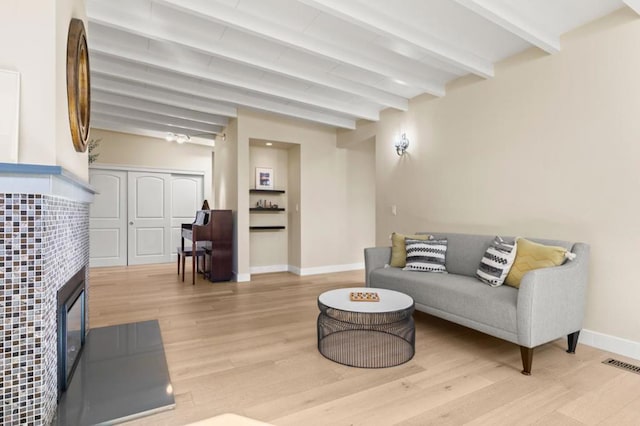 living room featuring beam ceiling, a fireplace, and light hardwood / wood-style flooring