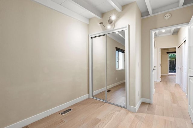 unfurnished bedroom featuring a closet, beam ceiling, and light hardwood / wood-style flooring