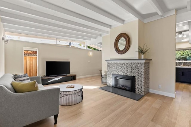 living room with a tiled fireplace, sink, light hardwood / wood-style flooring, and vaulted ceiling with beams