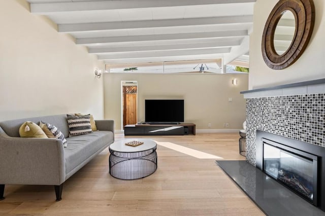 living room with lofted ceiling with beams, a tile fireplace, and light wood-type flooring