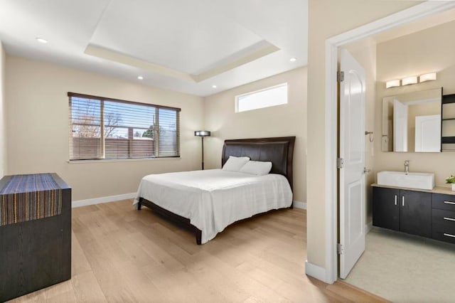 bedroom with sink, a tray ceiling, and light wood-type flooring