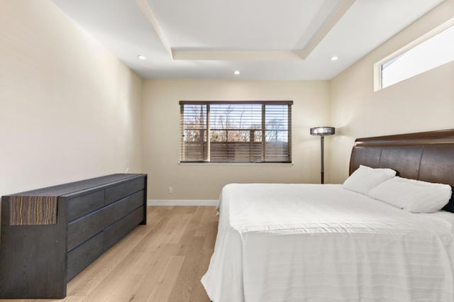 bedroom featuring multiple windows, light hardwood / wood-style flooring, and a raised ceiling