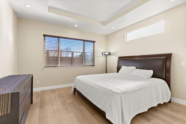 bedroom featuring multiple windows, a raised ceiling, and light wood-type flooring