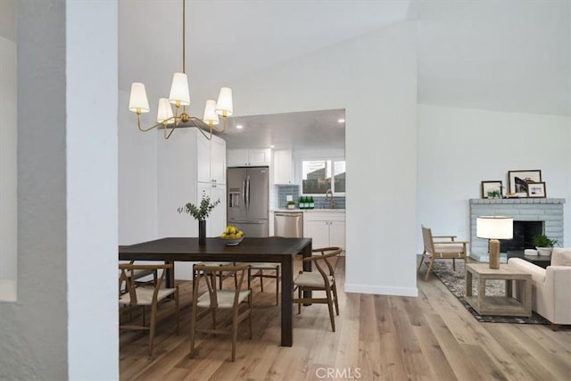 dining area with lofted ceiling, sink, a notable chandelier, light hardwood / wood-style floors, and a brick fireplace