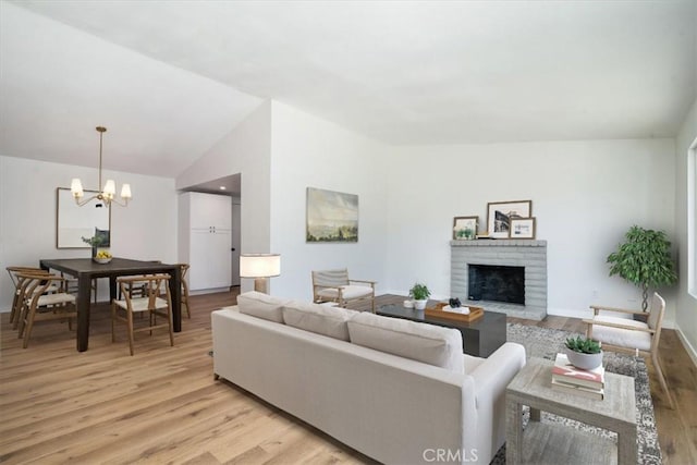 living room with lofted ceiling, a notable chandelier, a fireplace, and light wood-type flooring