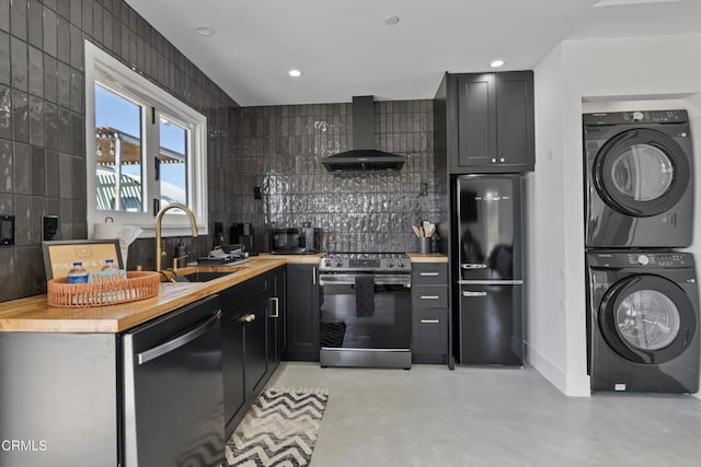 kitchen with stacked washer and clothes dryer, sink, wooden counters, wall chimney range hood, and black appliances