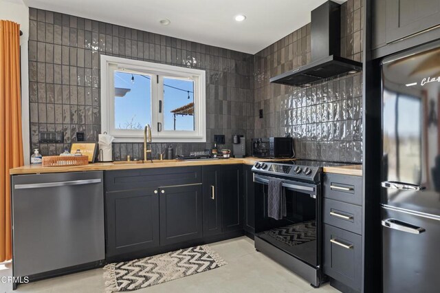 kitchen with wood counters, sink, appliances with stainless steel finishes, wall chimney range hood, and backsplash