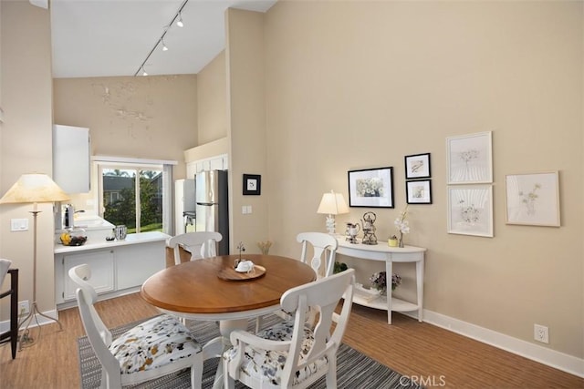 dining room with a towering ceiling, rail lighting, and light hardwood / wood-style floors