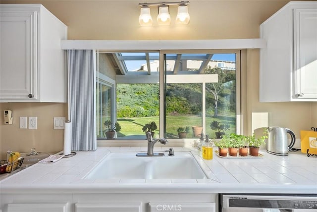 kitchen with tile counters, dishwasher, sink, and white cabinets