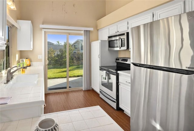 kitchen with sink, dark wood-type flooring, appliances with stainless steel finishes, white cabinetry, and tile countertops