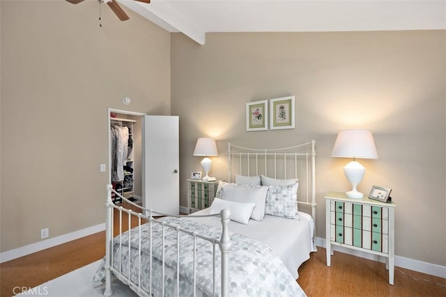 bedroom with a walk in closet, beam ceiling, wood-type flooring, and a closet