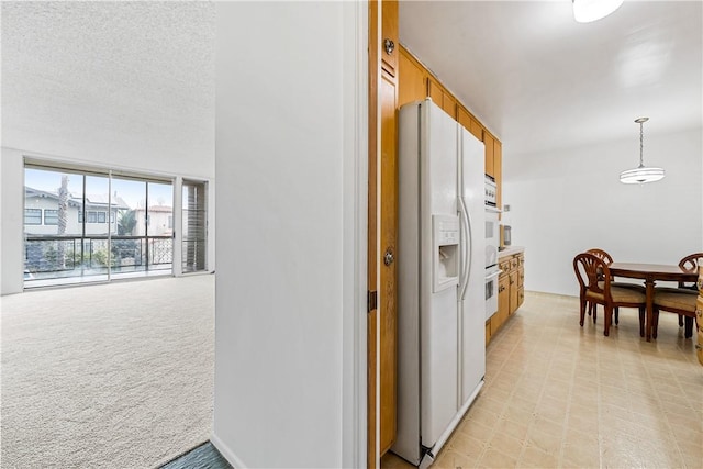 kitchen with white appliances, decorative light fixtures, light carpet, and a textured ceiling