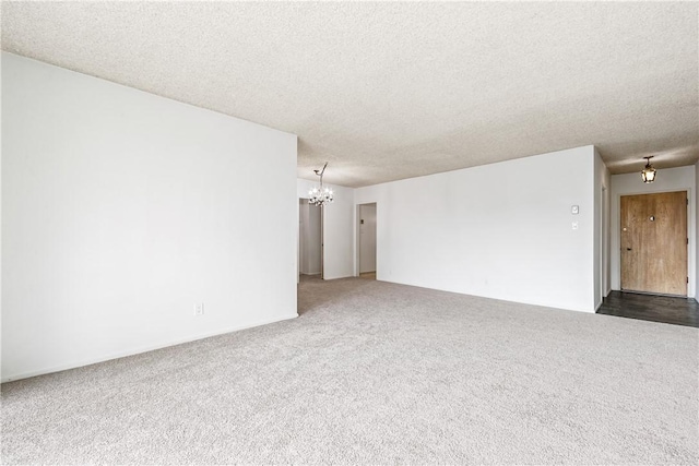 carpeted empty room featuring a textured ceiling and a chandelier