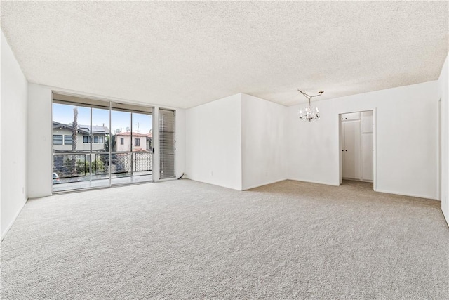 carpeted empty room featuring floor to ceiling windows, a notable chandelier, and a textured ceiling