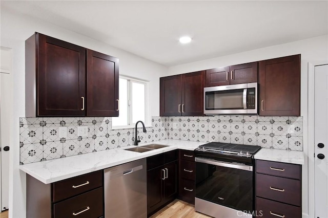 kitchen with sink, stainless steel appliances, light stone counters, decorative backsplash, and light wood-type flooring