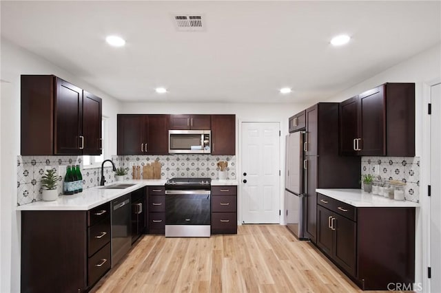 kitchen with sink, tasteful backsplash, dark brown cabinets, appliances with stainless steel finishes, and light hardwood / wood-style floors