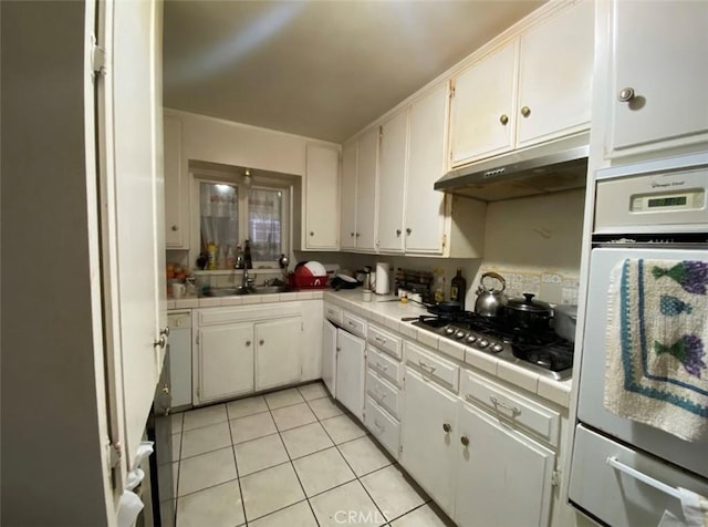 kitchen with white cabinets, light tile patterned flooring, tile counters, and oven