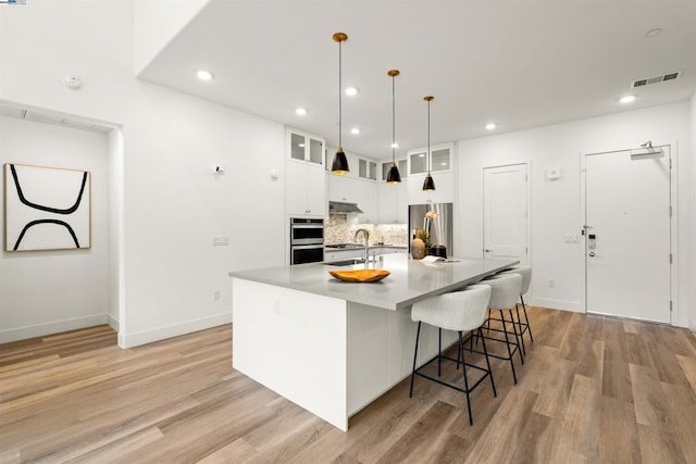 kitchen featuring sink, white cabinetry, light wood-type flooring, pendant lighting, and stainless steel appliances