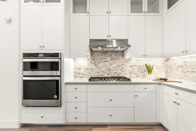 kitchen featuring appliances with stainless steel finishes, white cabinetry, dark hardwood / wood-style floors, tasteful backsplash, and extractor fan