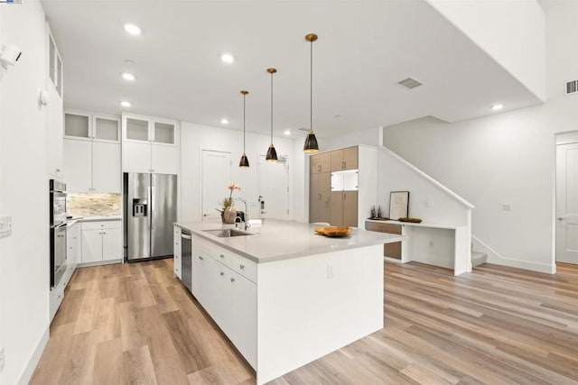 kitchen featuring sink, appliances with stainless steel finishes, white cabinetry, an island with sink, and decorative light fixtures