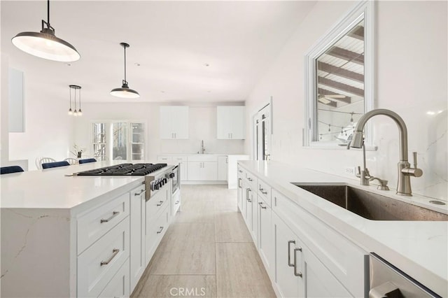 kitchen featuring stainless steel gas stovetop, white cabinetry, sink, and pendant lighting