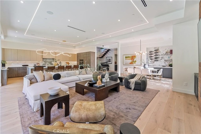 living room with an inviting chandelier, a tray ceiling, and light wood-type flooring