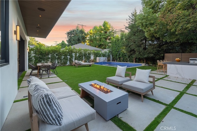 patio terrace at dusk featuring a yard, an outdoor living space with a fire pit, an outdoor bar, and pool water feature