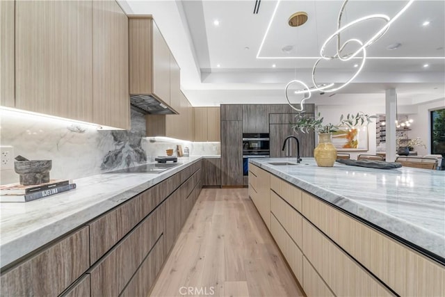 kitchen with sink, double wall oven, light stone countertops, black electric cooktop, and decorative light fixtures