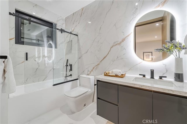 full bathroom with shower / bath combination with glass door, vanity, toilet, and tile walls