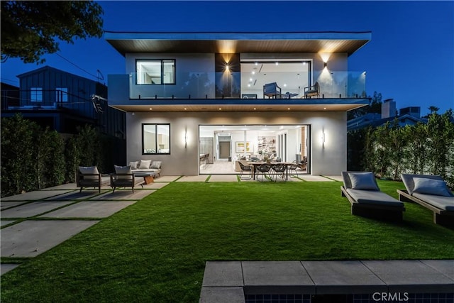 back house at night with a balcony, a yard, an outdoor living space, and a patio area