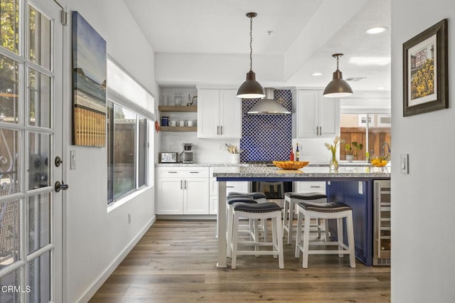 kitchen featuring wall chimney range hood, a breakfast bar, white cabinetry, tasteful backsplash, and decorative light fixtures