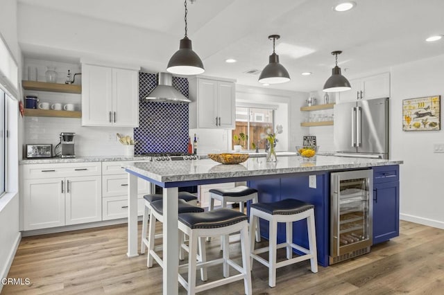 kitchen with decorative light fixtures, white cabinets, beverage cooler, stainless steel appliances, and wall chimney range hood