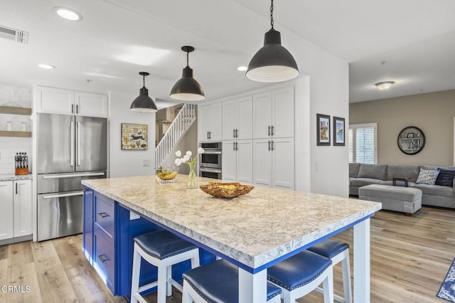 kitchen featuring a kitchen island, appliances with stainless steel finishes, decorative light fixtures, white cabinetry, and a breakfast bar area