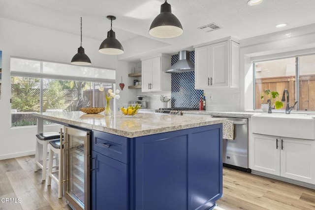 kitchen featuring decorative light fixtures, white cabinets, beverage cooler, stainless steel dishwasher, and wall chimney exhaust hood