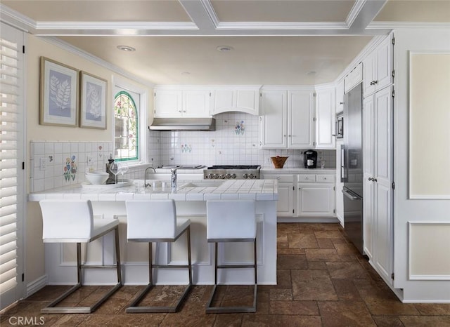 kitchen featuring under cabinet range hood, stone tile floors, a peninsula, a kitchen breakfast bar, and white cabinets