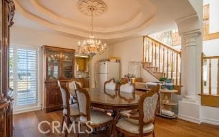 dining area with dark hardwood / wood-style floors, a raised ceiling, and decorative columns