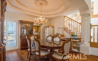 dining room featuring a tray ceiling, dark wood-type flooring, decorative columns, and a chandelier