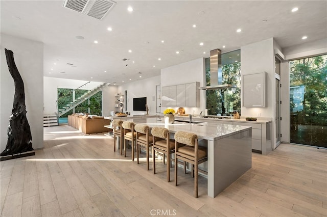 4727 Alonzo Ave, Encino, CA 91316 - kitchen with a kitchen bar, white cabinetry, light hardwood / wood-style flooring, a large island with sink, and wall chimney range hood