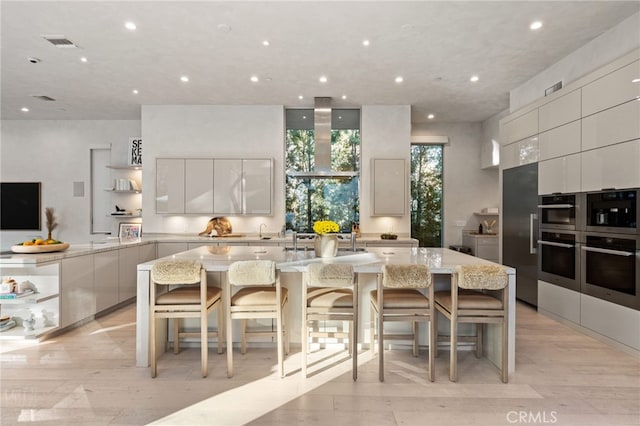 4727 Alonzo Ave, Encino, CA 91316 - kitchen with white cabinetry, a kitchen breakfast bar, light stone countertops, light wood-type flooring, and a spacious island
