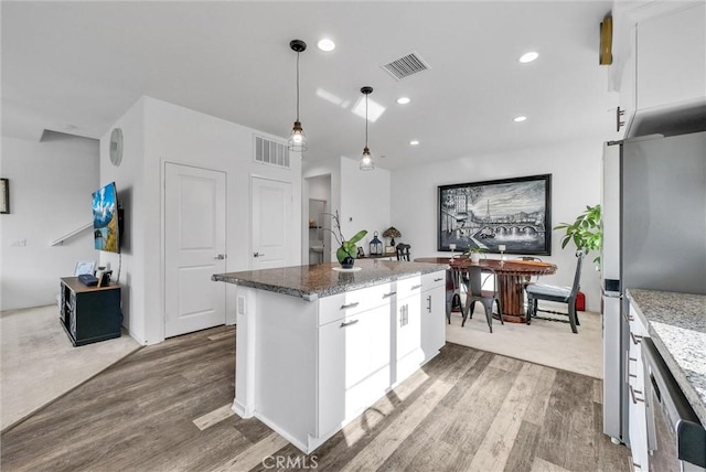 kitchen with white cabinetry, a kitchen island, light stone counters, and hanging light fixtures