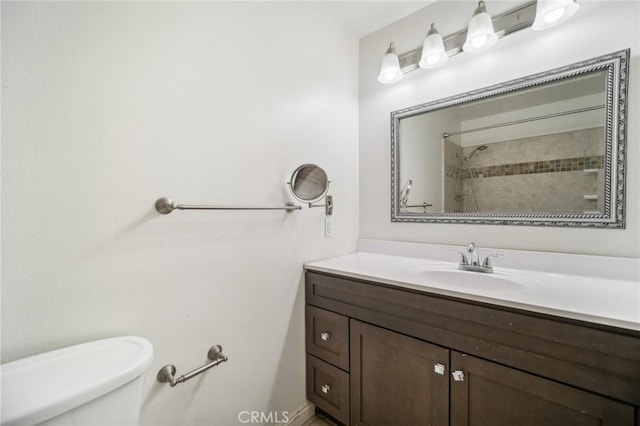 bathroom with a tile shower, vanity, and toilet