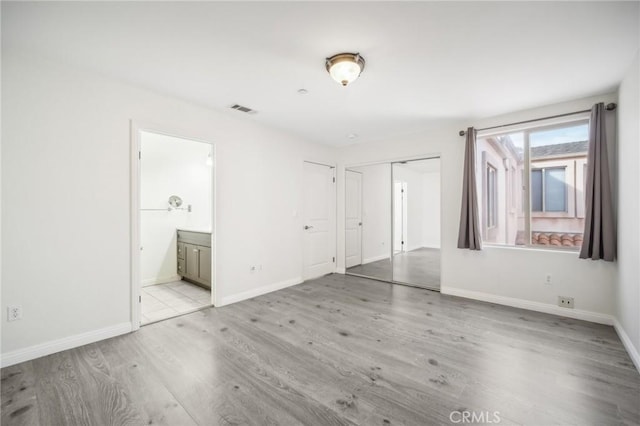 unfurnished bedroom with a closet, ensuite bathroom, and light hardwood / wood-style flooring