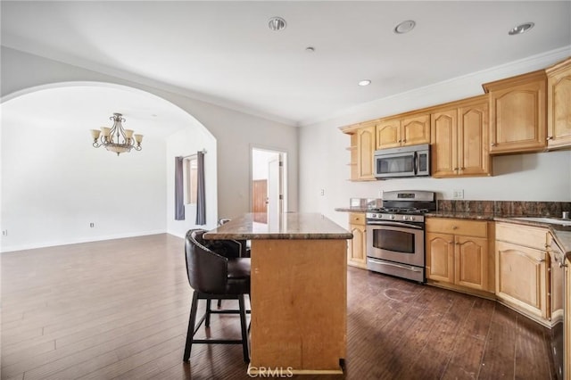 kitchen with a breakfast bar area, a center island, ornamental molding, appliances with stainless steel finishes, and dark hardwood / wood-style floors