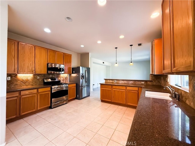 kitchen with sink, dark stone countertops, hanging light fixtures, stainless steel appliances, and tasteful backsplash