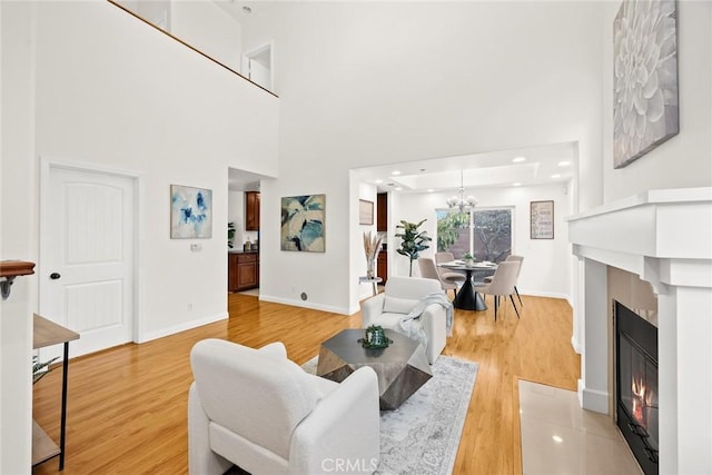 living room with an inviting chandelier, a towering ceiling, a fireplace, and wood-type flooring