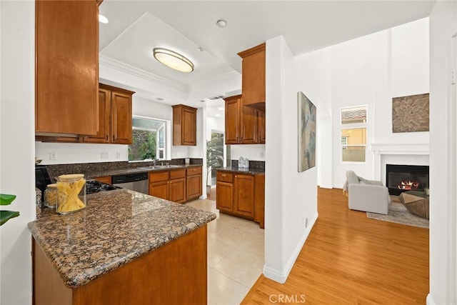 kitchen featuring sink, dark stone countertops, a tray ceiling, dishwasher, and light hardwood / wood-style floors